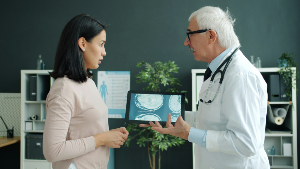 Neurologista analisando eletroencefalograma ao lado de familiar de paciente durante consulta de diagnóstico de epilepsia.